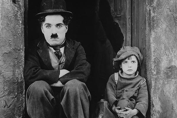 Charlie Chaplin mit Melone und Schnurrbart neben einem ernst blickenden Kind
