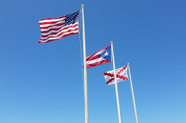 Fahnenmasten mit der Flagge Puerto Ricos und weiteren Flaggen vor blauem Himmel